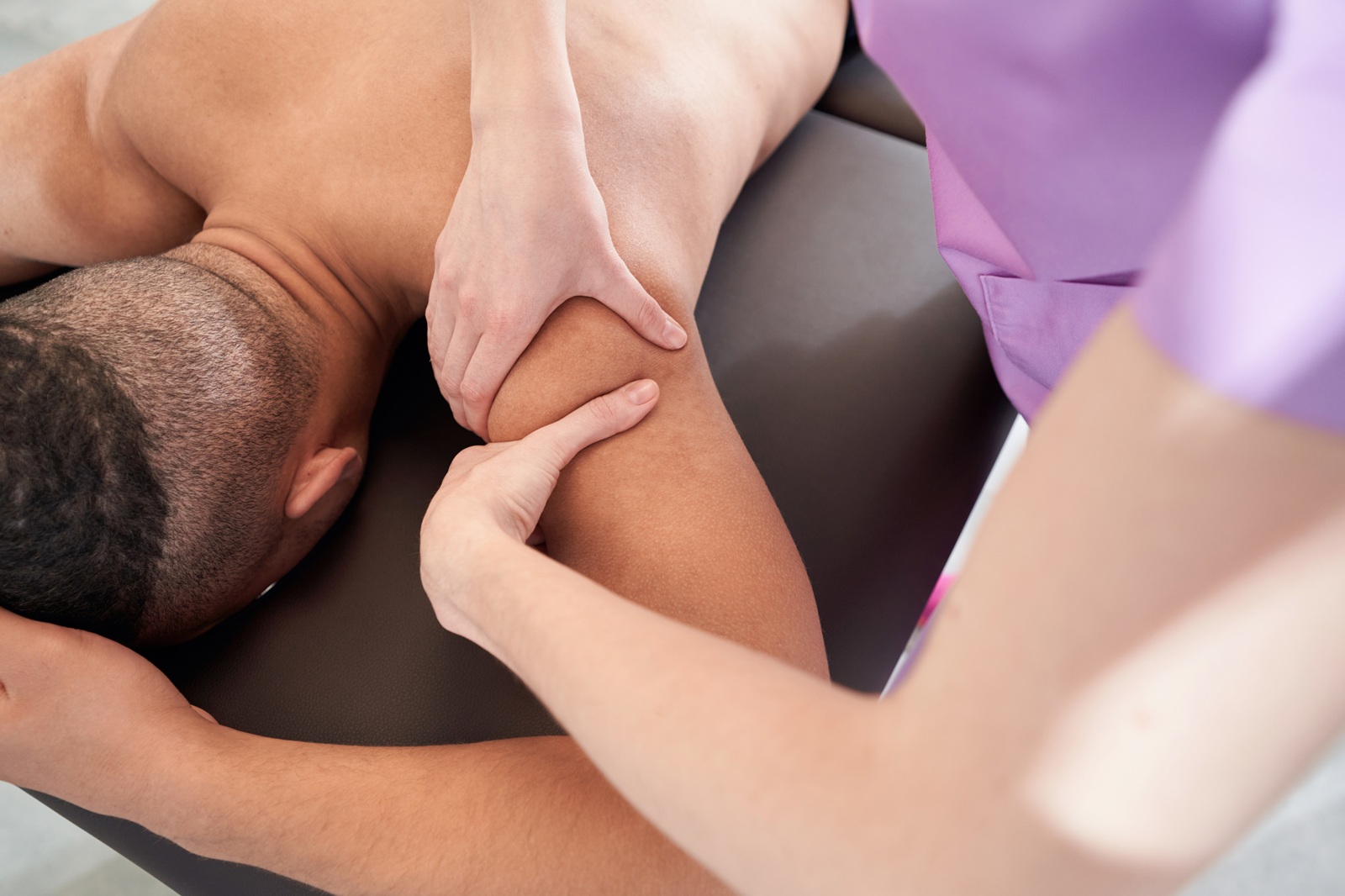 Close up of African American man lying on massage table while professional masseuse massaging male arm