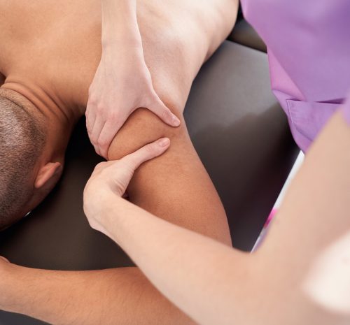 Close up of African American man lying on massage table while professional masseuse massaging male arm